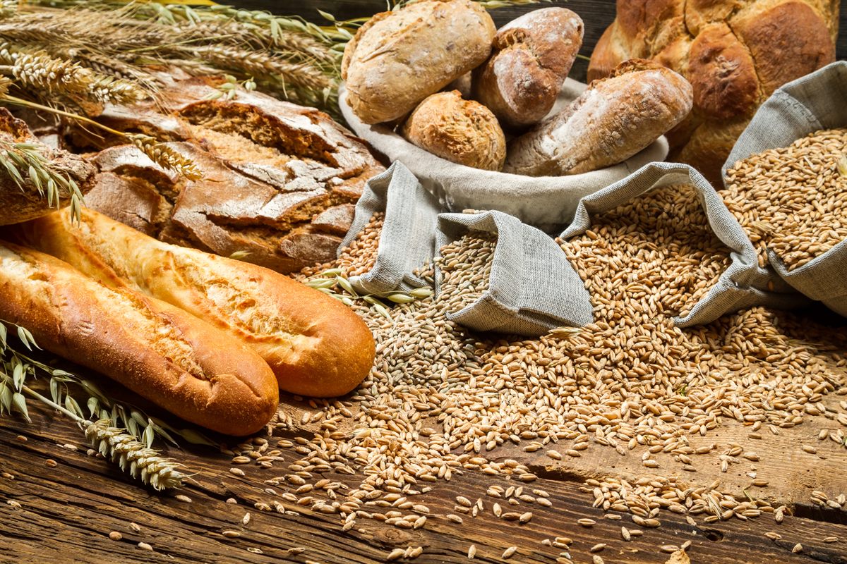 Frisches Brot und Brötchen neben Leinensäcken mit Getreidekörnern und Ähren auf einem Holztisch